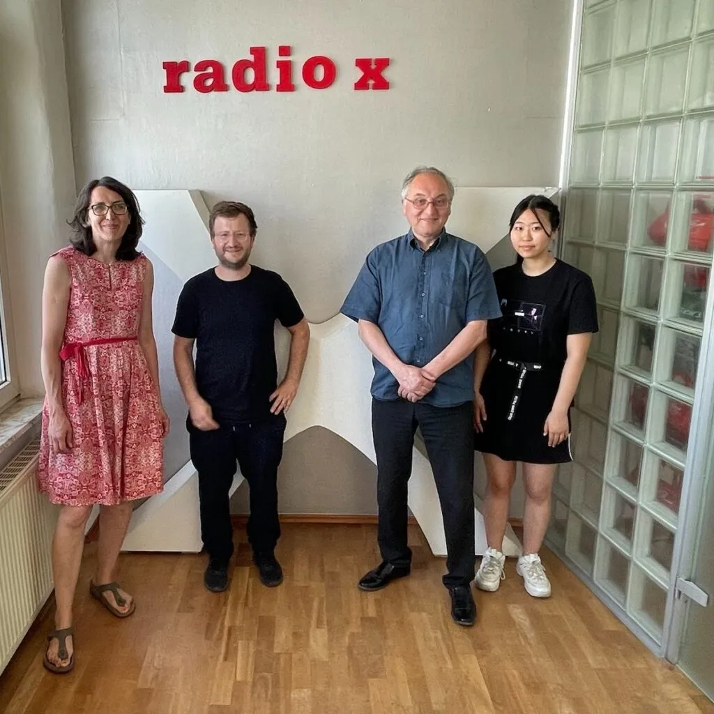 Anne und Jonathan von AdAptiv stehen zusammen mit Winfried Becker und einer Mitarbeiterin von Radio x vor dem Logo des Senders