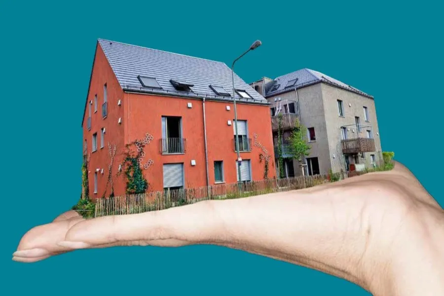 Fotomontage von einer flachen Hand auf der zwei Häuser stehen